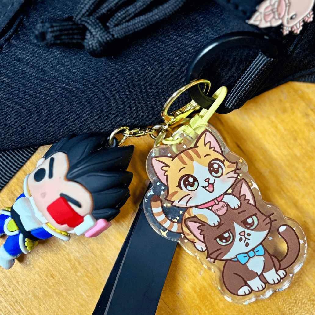 Double-sided acrylic keychain of Coqui and Frankie chibi, holographic stars, gold clasp.