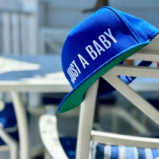 Blue snapback with green bill that says "Just a Baby" by Frankie Said Meow