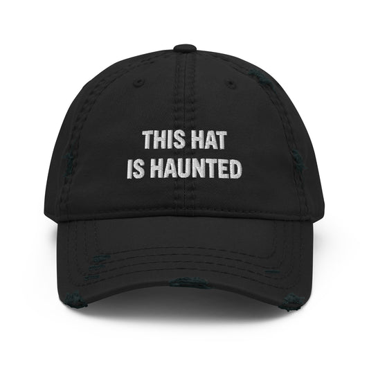 Distressed dad hat in black with white embroidered text reading “this hat is haunted.”