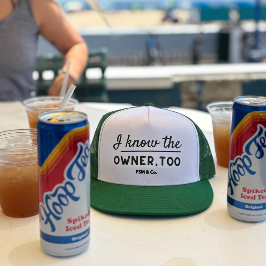 Green and white trucker hat "I know the owner, too" with Hoop Tea on the boardwalk