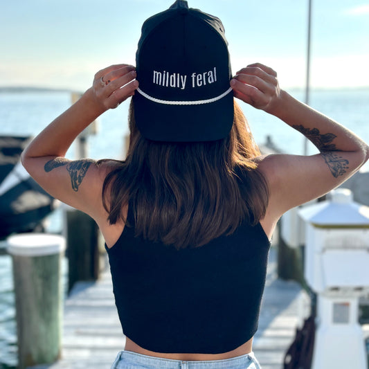 woman on dock wearing black "Mildly Feral" rope hat backwards